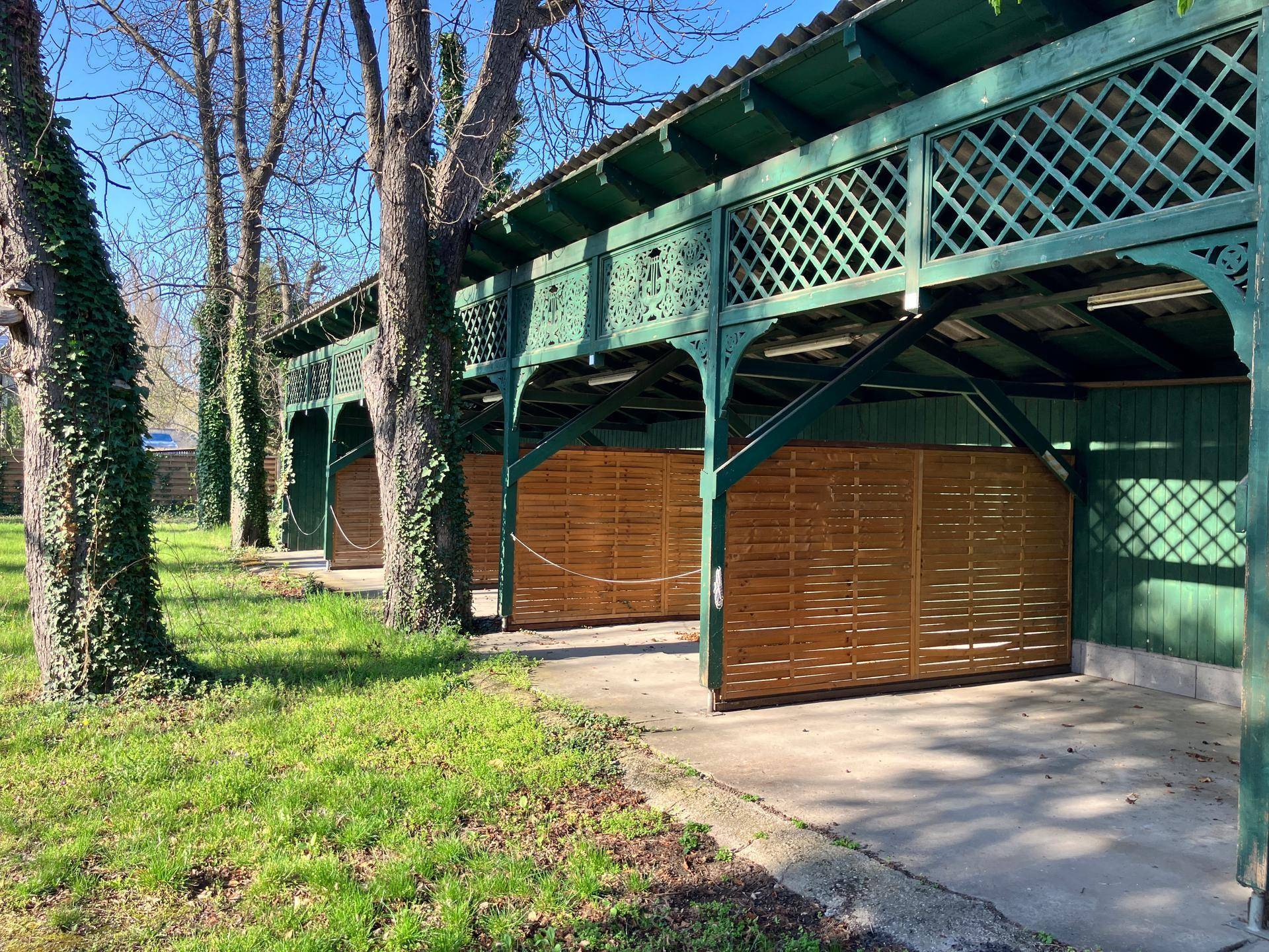 Grüne Holzkonstruktion mit dekorativen Gittern, die als überdachter Parkplatz oder Carport dient.