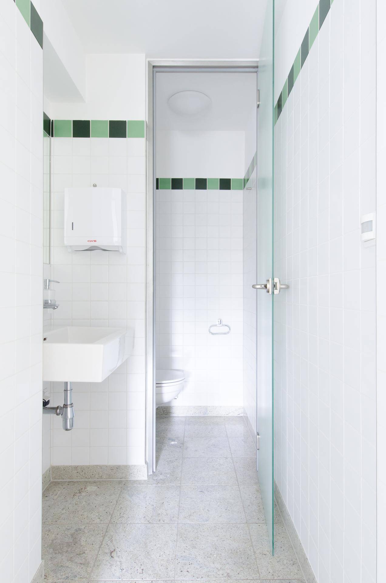Ein sauberer Toilettenraum mit weißen Fliesen, einem Waschbecken und grünen Akzenten.