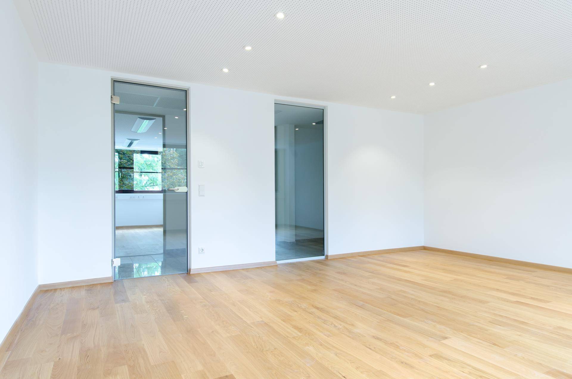 Ein heller Büroraum mit hellem Holzparkett und modernen Glastüren, die den Raum unterteilen.