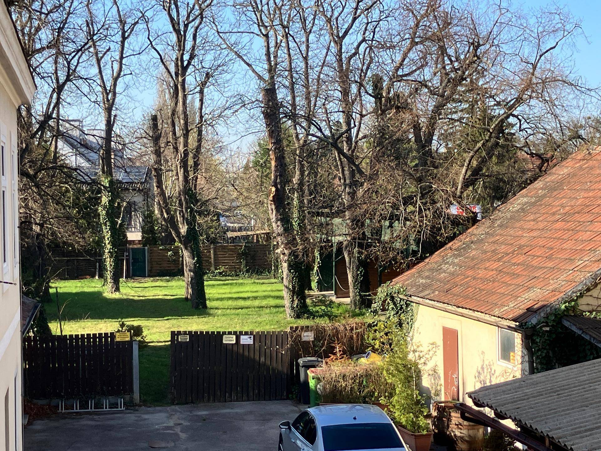 Weitläufiger Blick auf eine grüne Wiese mit vielen Bäumen und einem kleinen Gebäude mit rotem Dach.