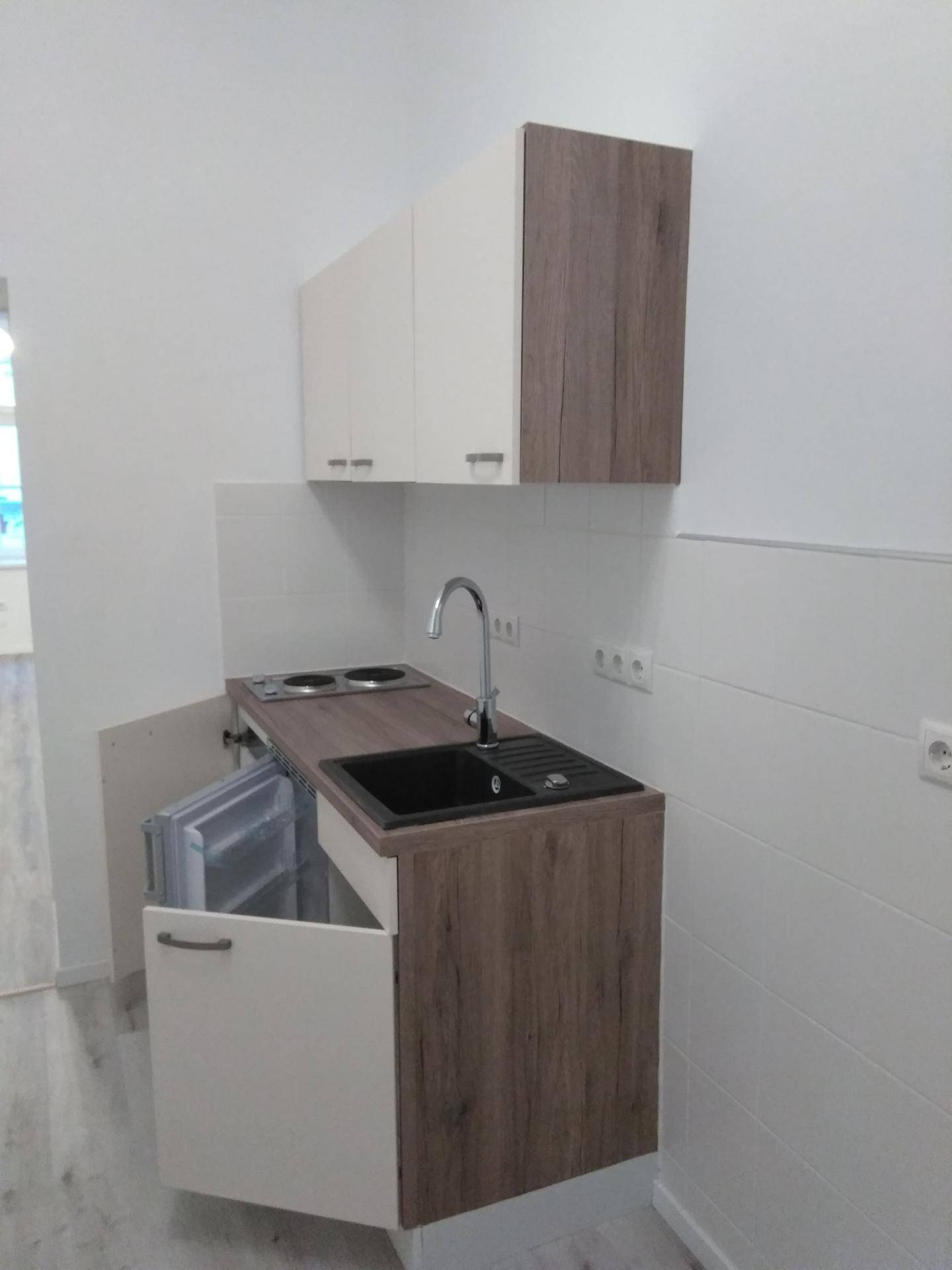 Kompakte Kochnische mit Spüle, zwei Kochplatten und integriertem Kühlschrank.