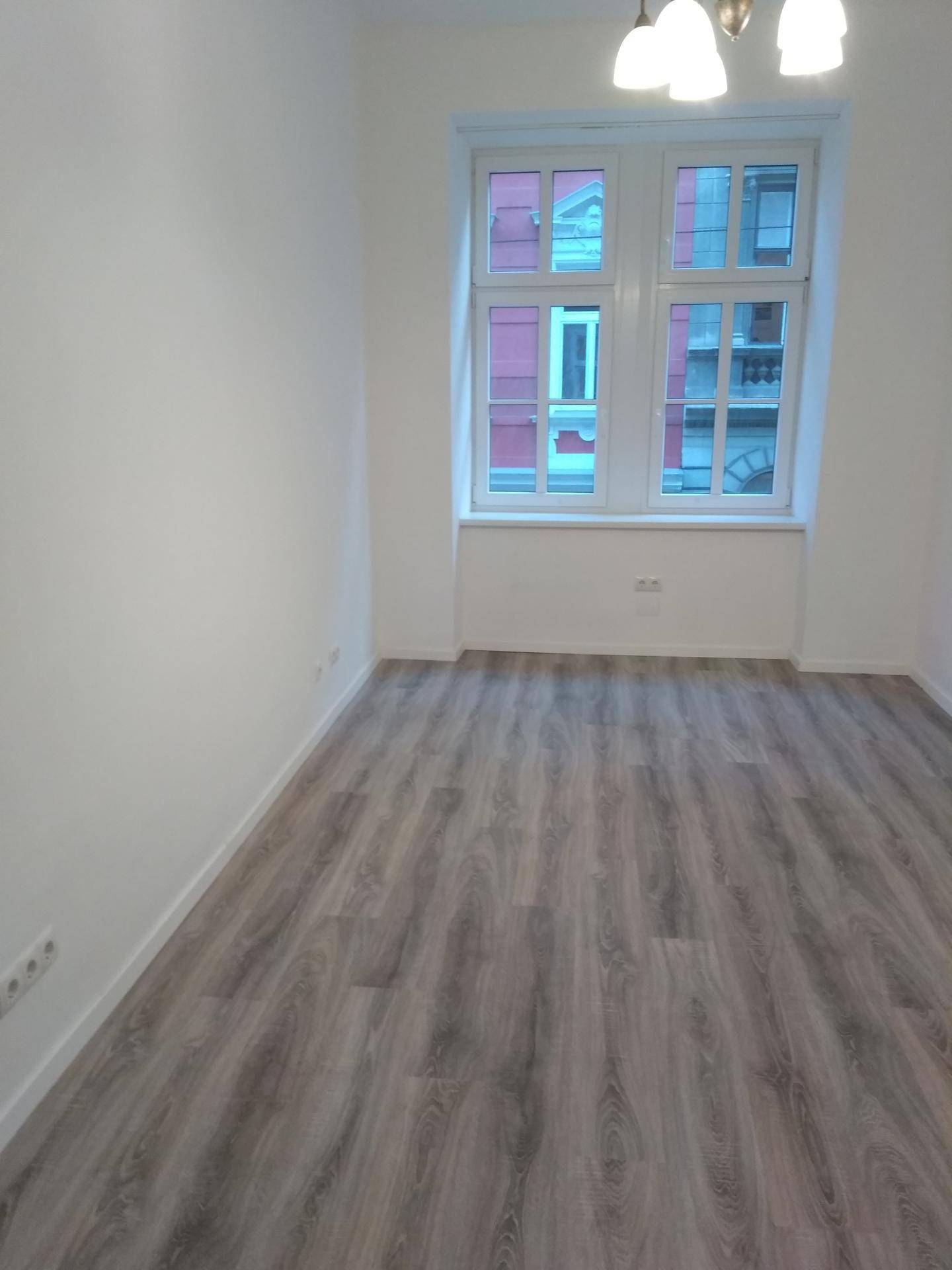Heller, leerer Raum mit großem Fenster und Laminatboden, ideal als Wohn- oder Schlafbereich.