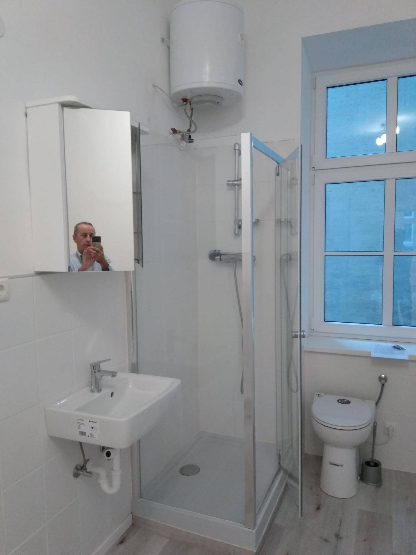 Modernes Badezimmer mit Dusche, Waschbecken, Toilette und Fenster für Tageslicht.
