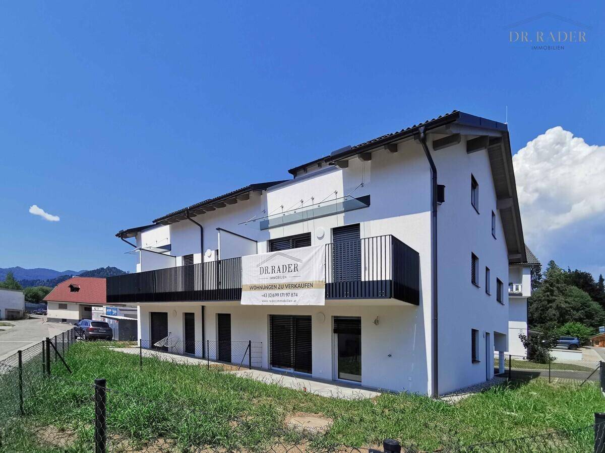 Neubau-Mehrfamilienhaus mit klaren Linien, weißen Wänden und dunklen Balkongeländern unter strahlendem Himmel.