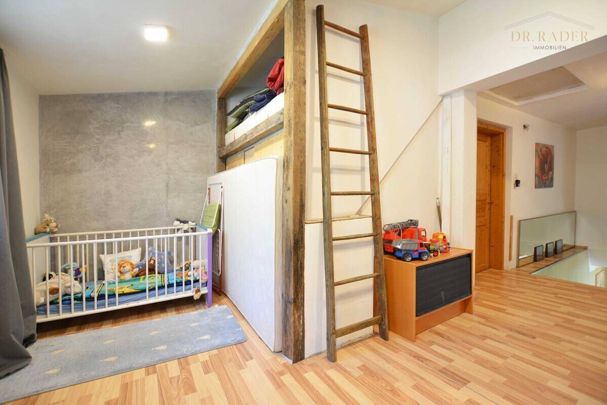 Kinderzimmer mit Holzboden, Hochbett und Babybett, unter einer Dachschräge.