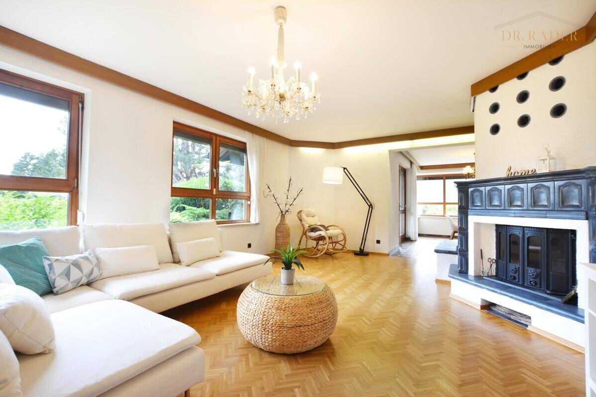 Geräumiges Wohnzimmer mit Kachelofen, Parkettboden und Zugang zu weiteren hellen Räumen.