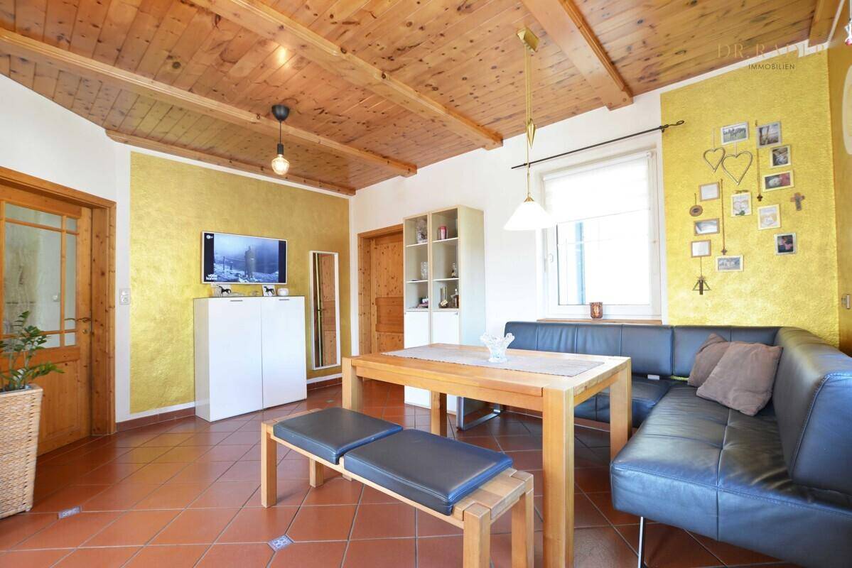 Essbereich mit Holztisch, Eckbank und sichtbarer Holzdecke, dekoriert mit gelber Akzentwand.