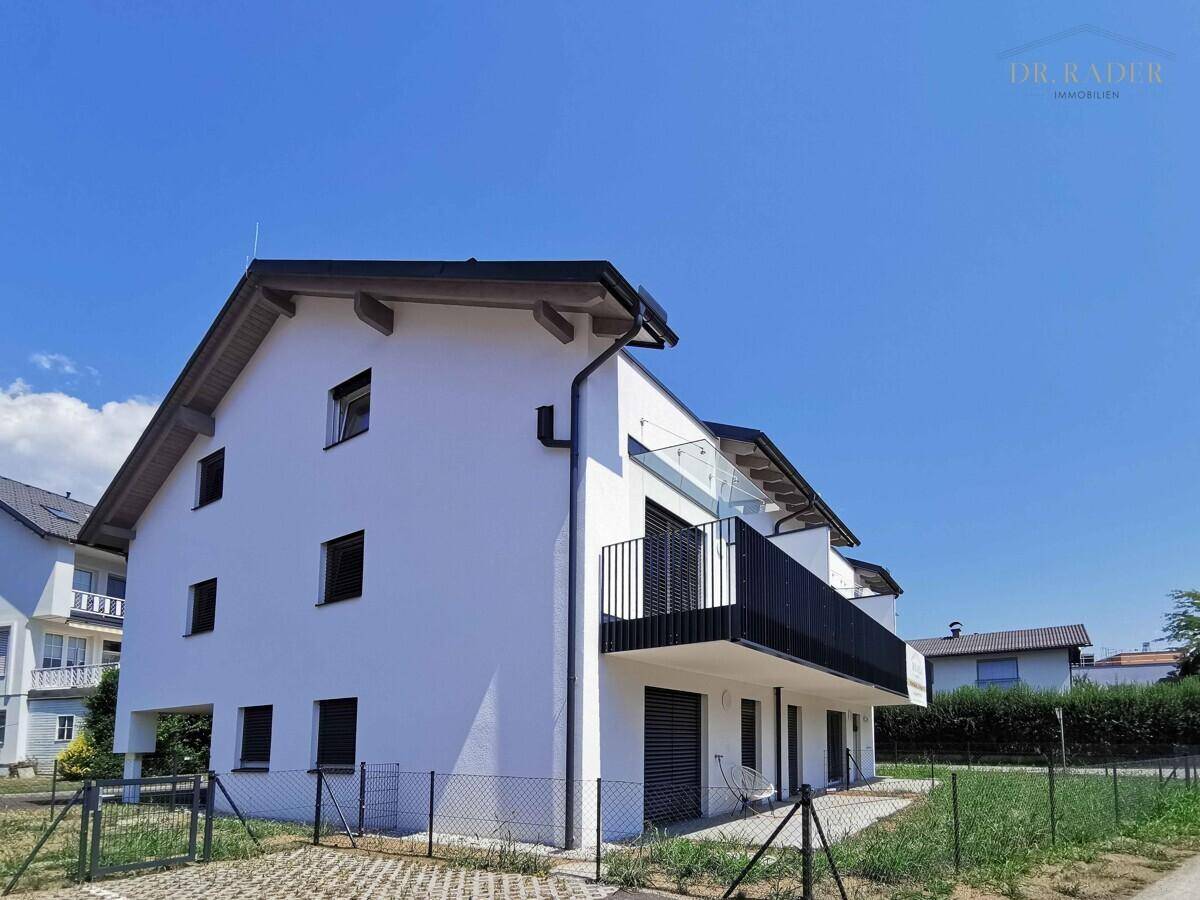 Seitenansicht eines modernen Neubaus mit weißer Fassade, Satteldach und einem Balkon unter klarem Himmel.