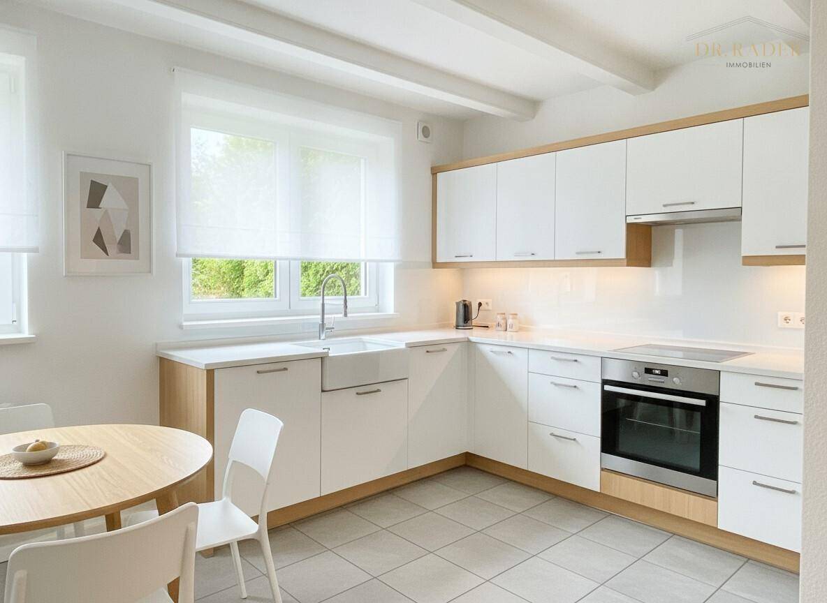 Moderne Küche mit weißen Schränken, hellem Fliesenboden und kleinem Essbereich am Fenster.