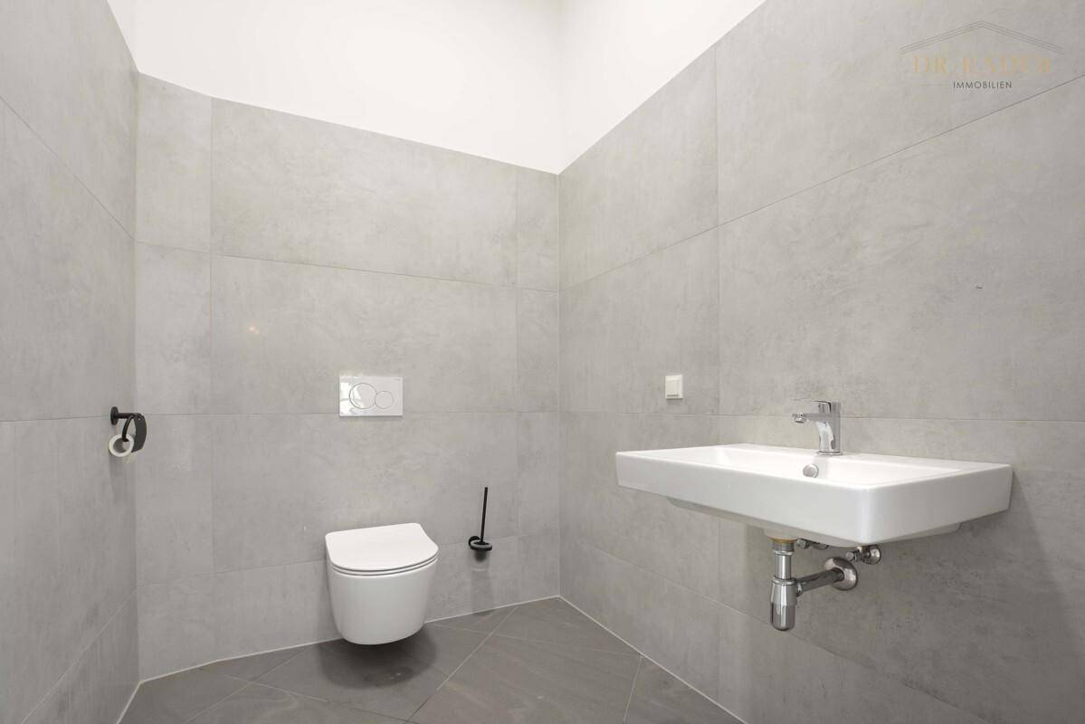 Modernes Gäste-WC mit wandhängender Toilette, Waschbecken und großformatigen grauen Fliesen.