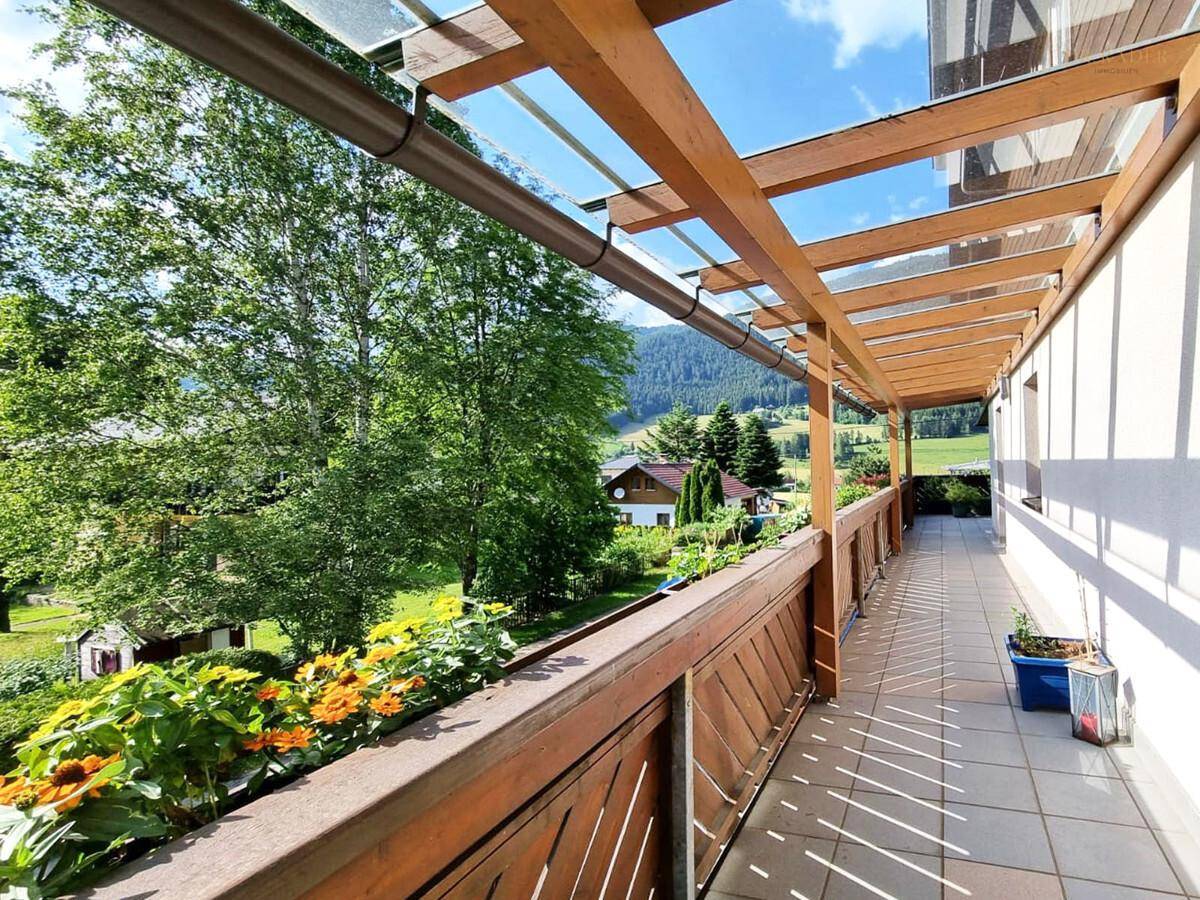 Langer, überdachter Balkon mit Blumenkästen und Bergblick.