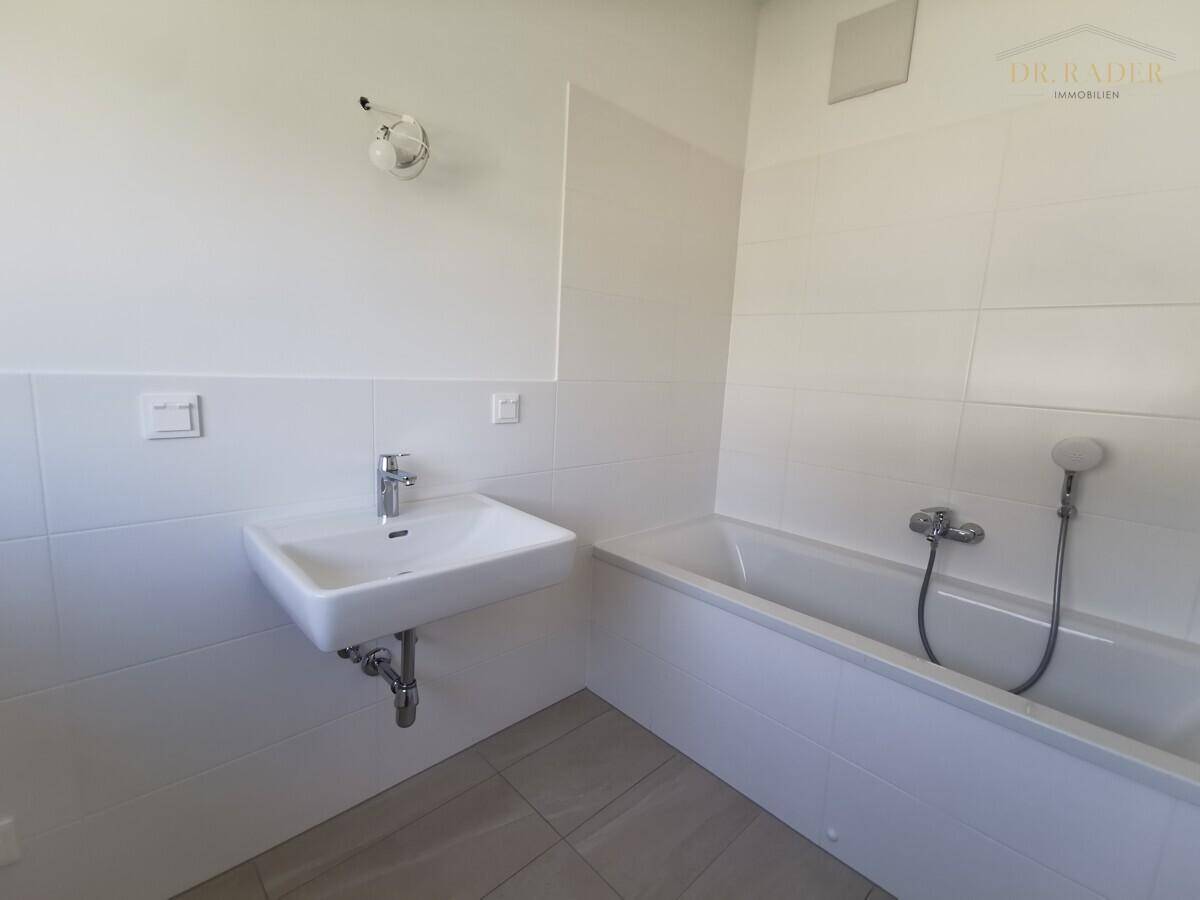Unmöbliertes Badezimmer mit weißen Fliesen, einer Badewanne und einem einzelnen Waschbecken.