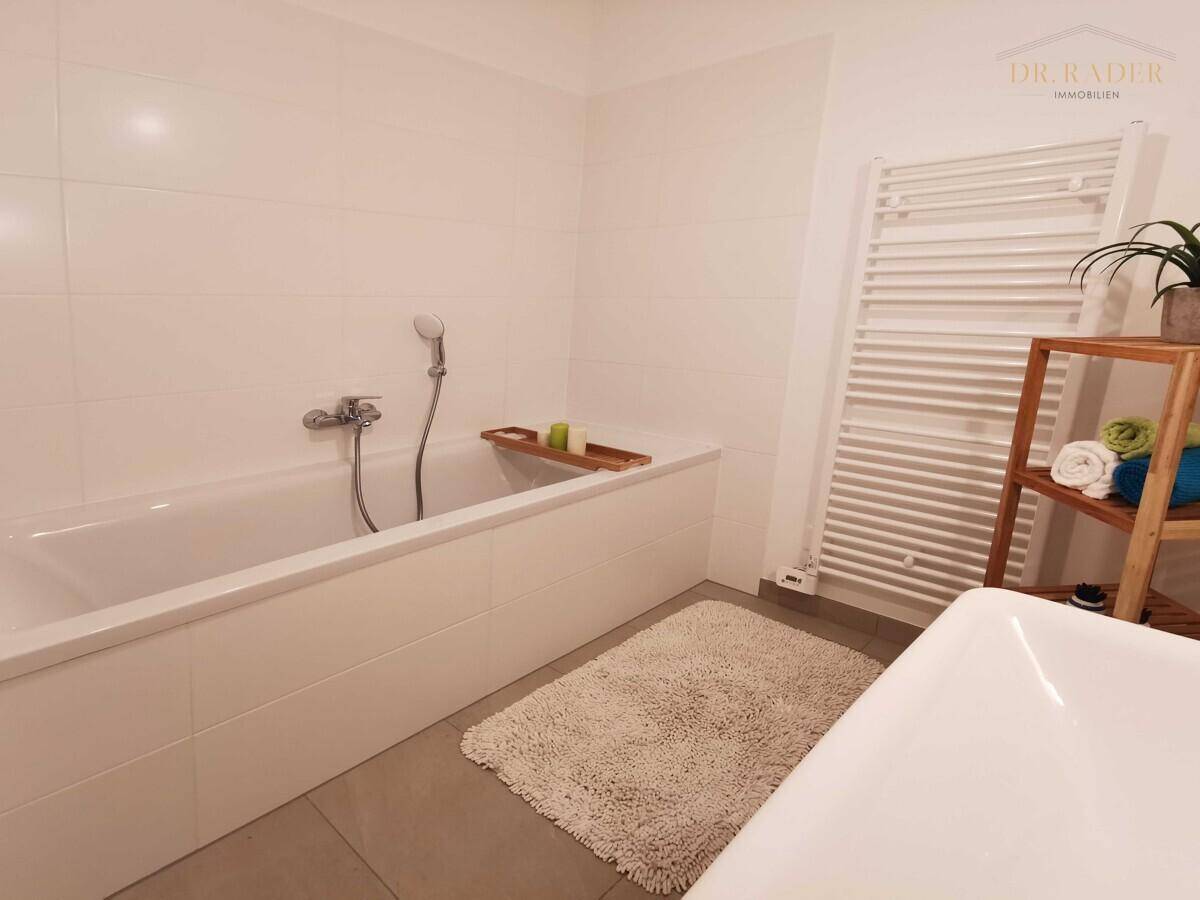 Helles, modernes Badezimmer mit integrierter Badewanne, weißen Wandfliesen und praktischem Handtuchheizkörper.