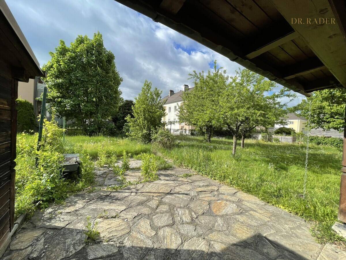 Rustikale Steinterrasse mit Holzdach und Blick auf den weitläufigen Gartenbereich.