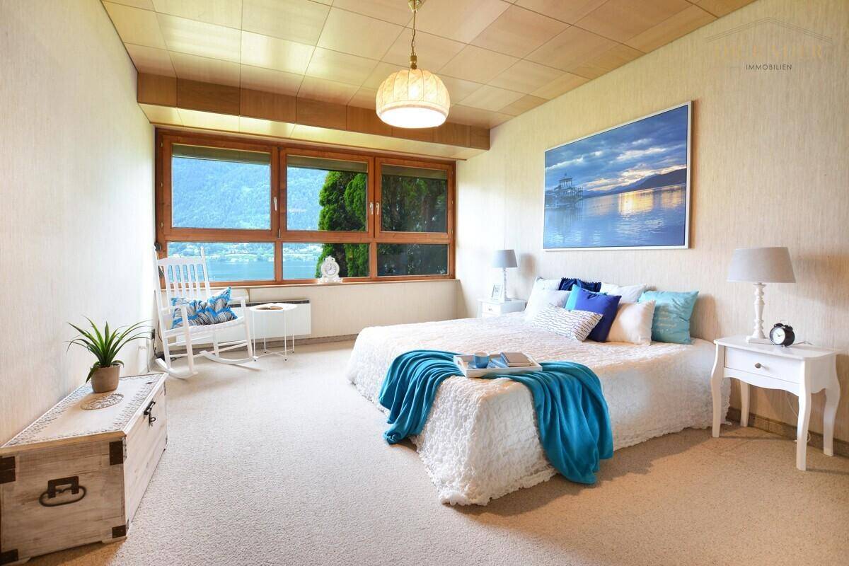 Helles Schlafzimmer mit Teppichboden, großem Fenster und malerischem Seeblick.