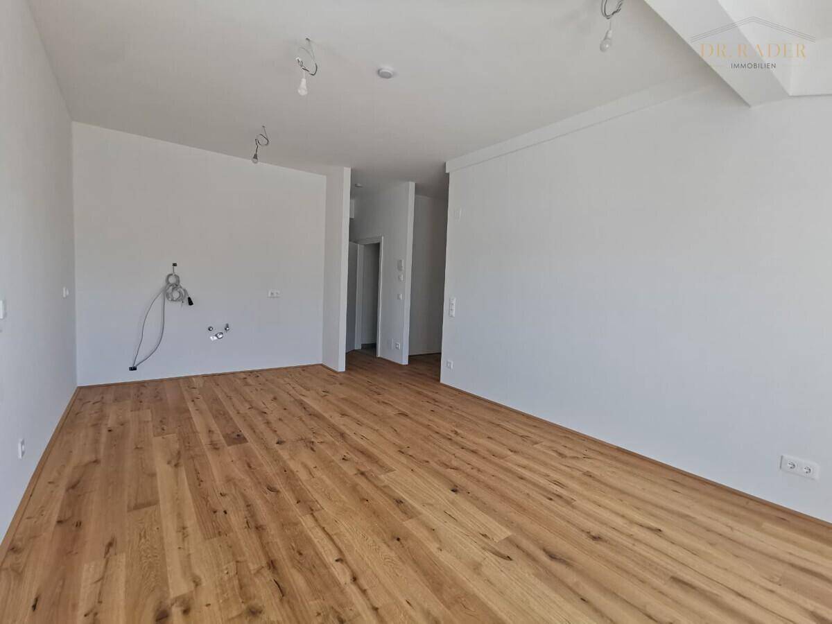 Geräumiger, heller Raum mit Holzboden und Zugang zu weiteren Zimmern, ideal als Wohnbereich.