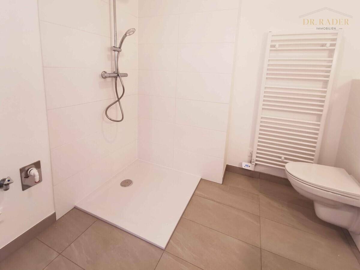 Modernes Badezimmer mit ebenerdiger Dusche, wandhängendem WC und beheiztem Handtuchhalter.