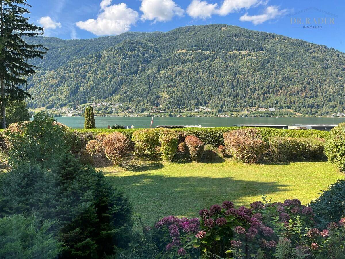 Gepflegte Rasenfläche mit Hecken und weitem Blick auf den See und die umliegende Berglandschaft.
