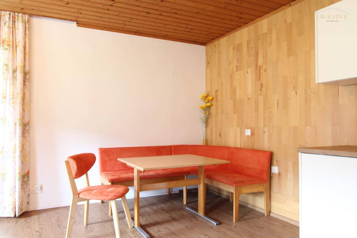 Essbereich mit orangefarbener Eckbank und Holztisch unter einer Holzdecke.