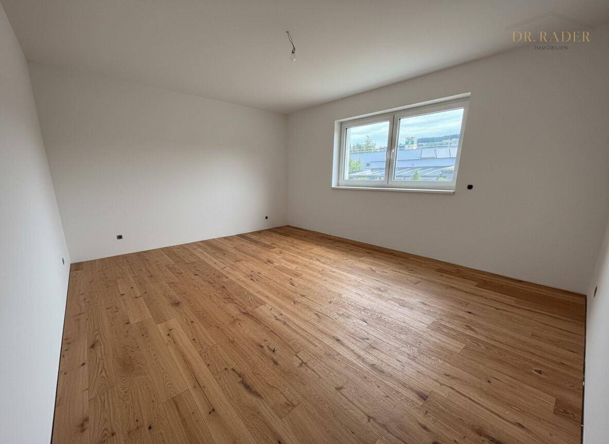 Unmöbliertes Schlafzimmer mit hellem Holzboden und großem Fenster, bereit zur Einrichtung.