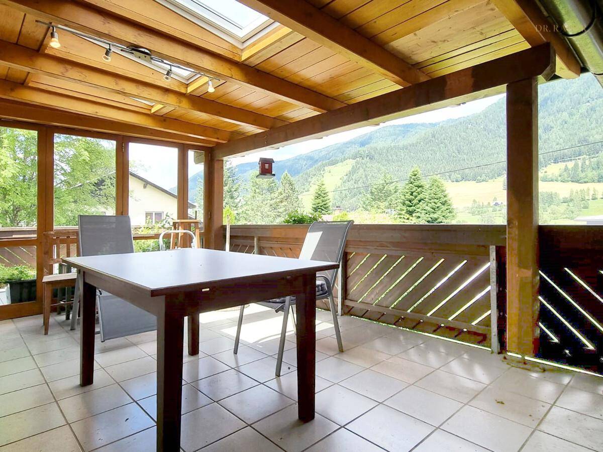 Heller Wintergarten mit Holzdach, Esstisch und Panoramablick auf die Berge.