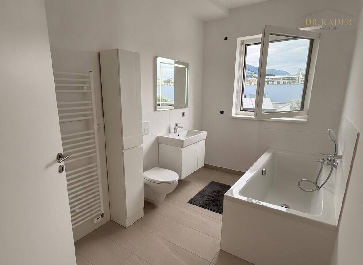 Helles Badezimmer mit Badewanne, WC, Waschbecken, Spiegelschrank und beheiztem Handtuchhalter.