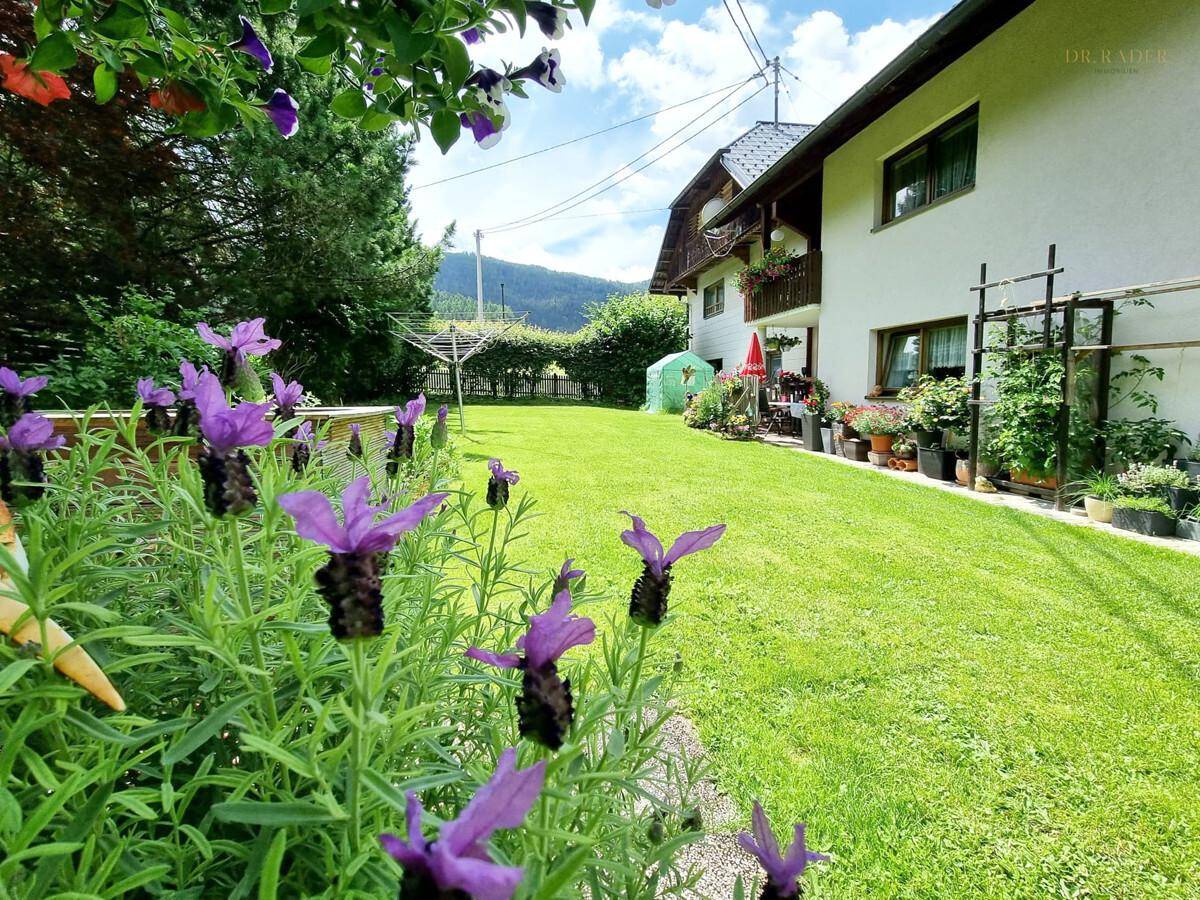 Blühender Garten mit Rasenfläche und Hausfassade im Hintergrund.