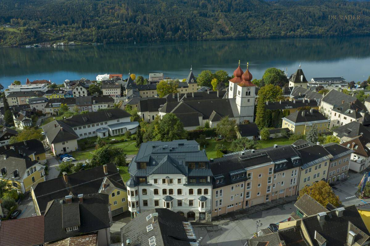 Luftaufnahme einer charmanten Stadt am See, umgeben von Bergen, mit historischen Gebäuden und viel Grün.
