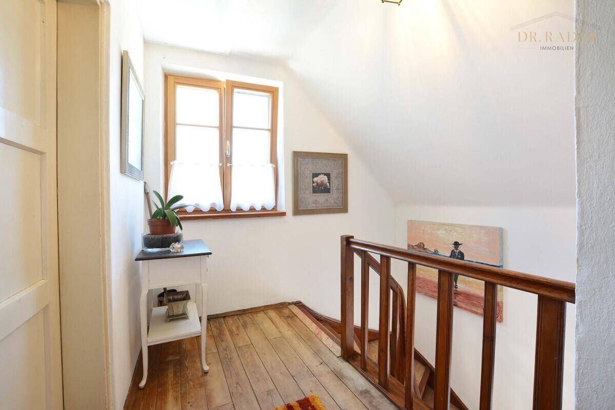 Oberer Flurbereich mit Holzboden, Fenster und kleiner Ablagefläche.