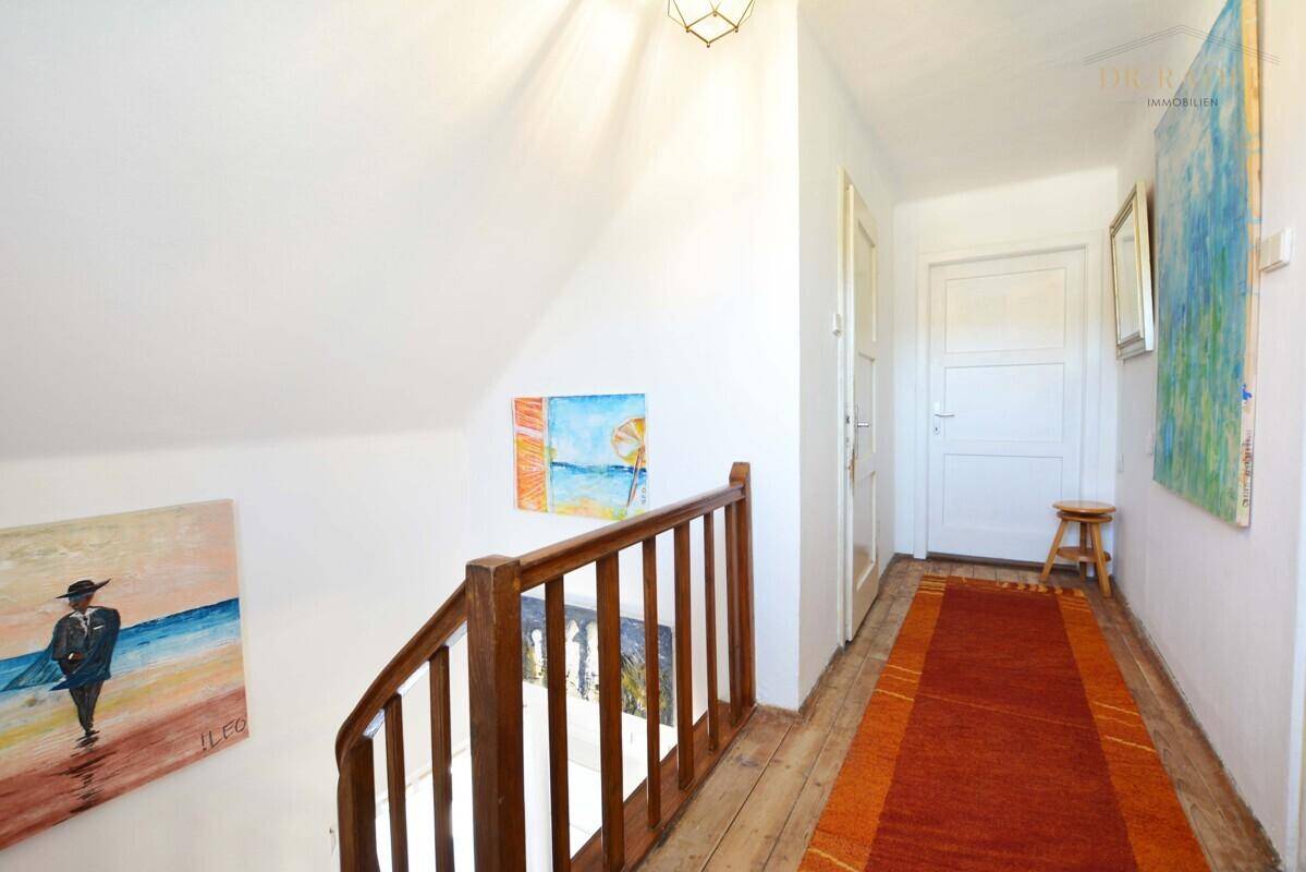 Heller Flur mit Holztreppe, Holzboden und farbenfrohen Kunstwerken an den Wänden.