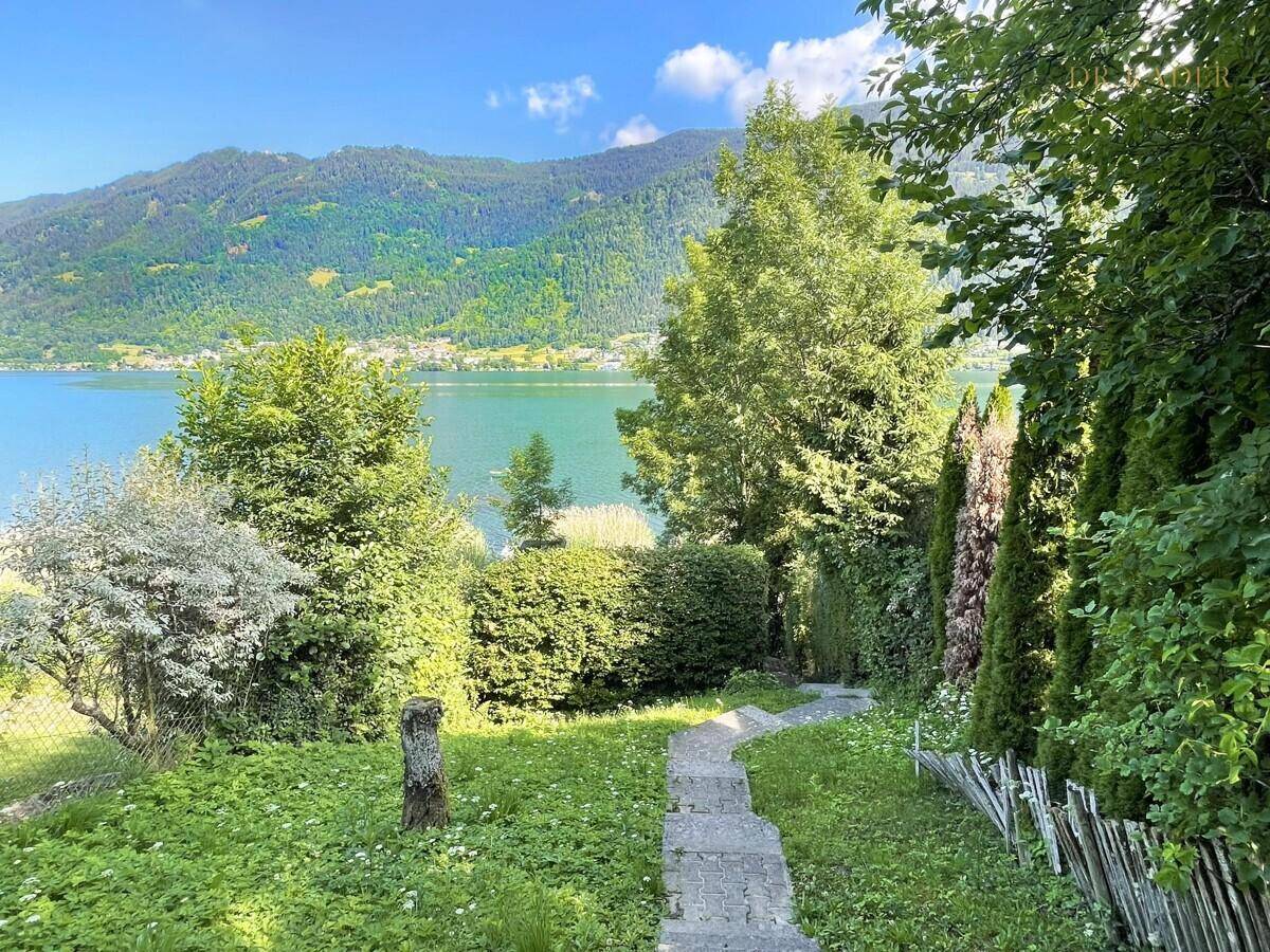 Grüner Garten mit Steinweg und weitem Blick auf den See und die bewaldeten Berge.