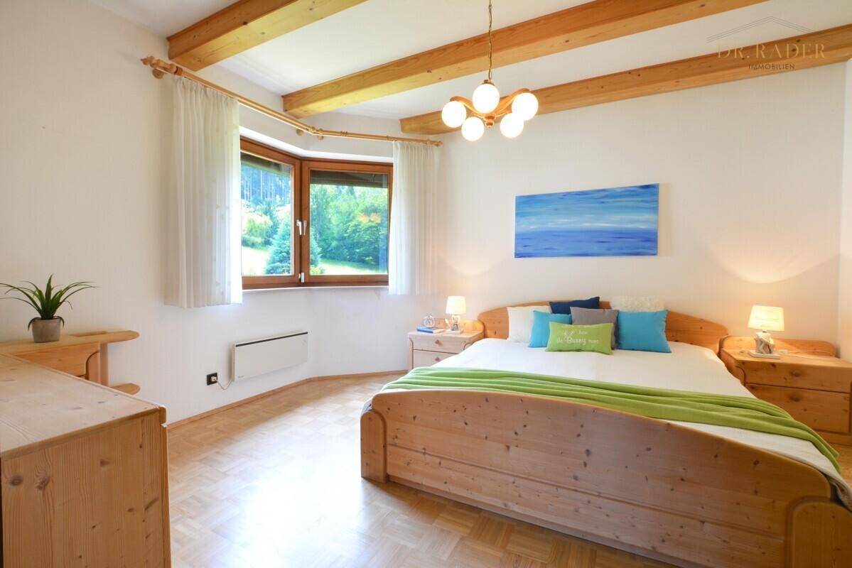 Gemütliches Schlafzimmer mit Holzbalken, Parkettboden und Fenster mit Blick ins Grüne.