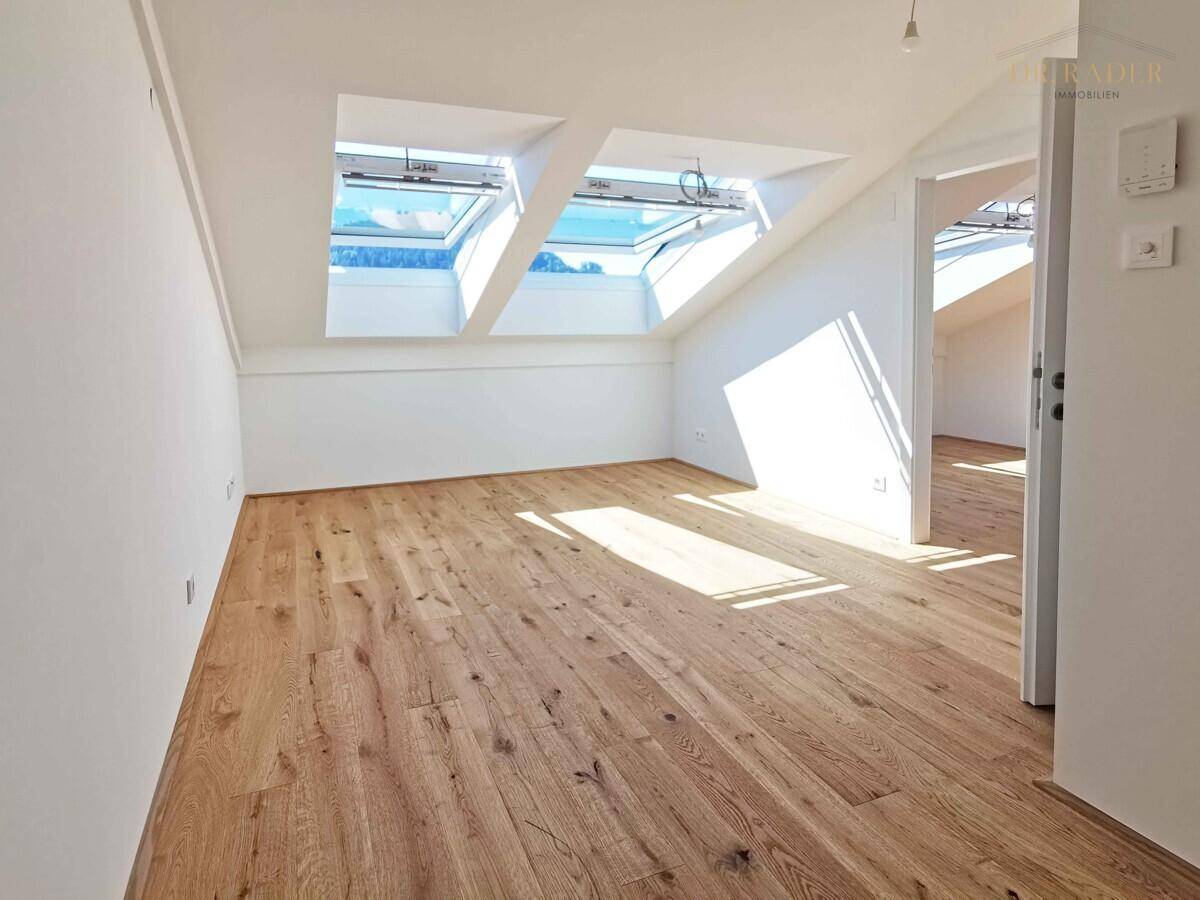 Heller Raum im Dachgeschoss mit Holzboden, schrägen Wänden und mehreren Dachfenstern.