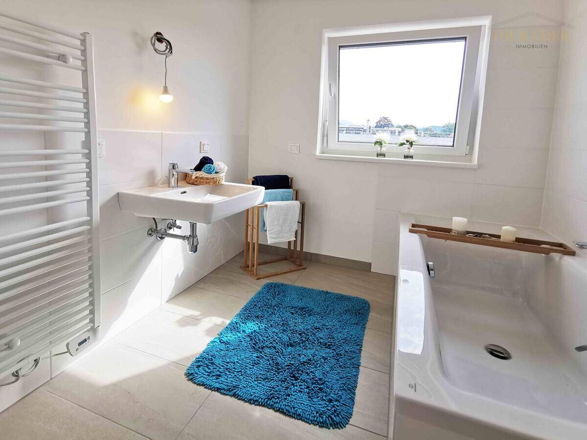 Modernes Badezimmer mit Badewanne, Waschbecken, beheiztem Handtuchhalter und Fenster.