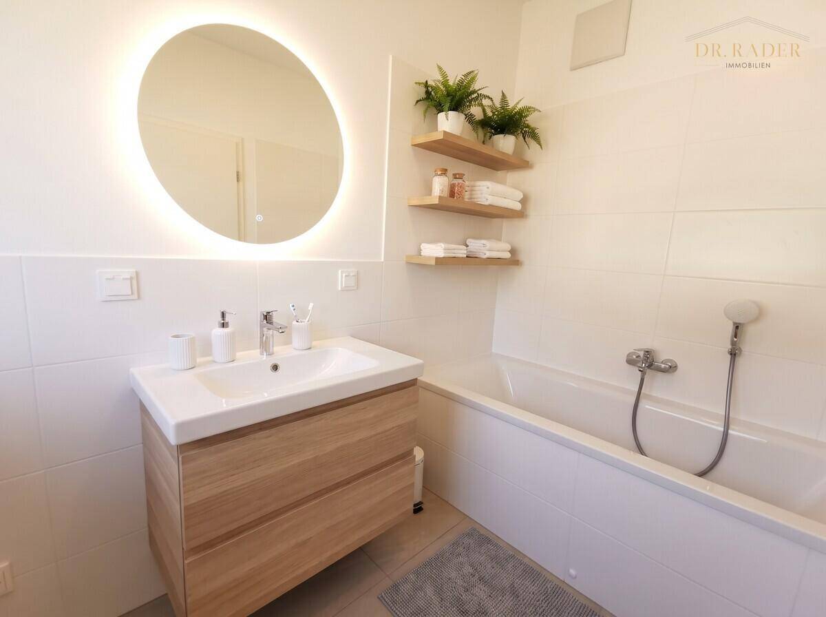 Modernes Badezimmer mit Badewanne, Waschtischunterschrank und beleuchtetem Spiegel.