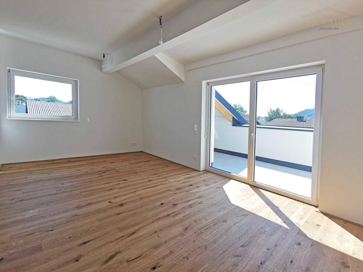 Heller Raum mit Holzboden, Dachschräge und großem Fenster mit Zugang zu einer Terrasse.