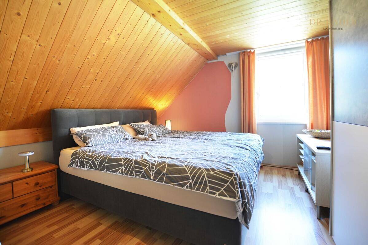 Gemütliches Schlafzimmer mit Holzboden, Dachschräge und sichtbarer Holzdecke.