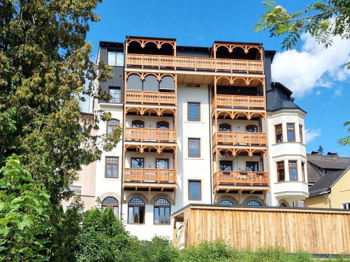 Renoviertes historisches Gebäude mit vielen Holzbalkonen und modernen Fenstern unter blauem Himmel.