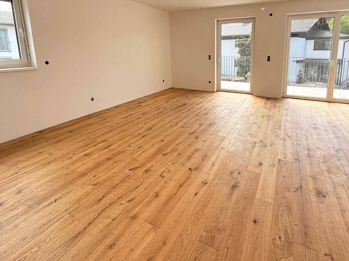 Geräumiger, unmöblierter Raum mit Holzboden und mehreren Zugängen zu einem Außenbereich.