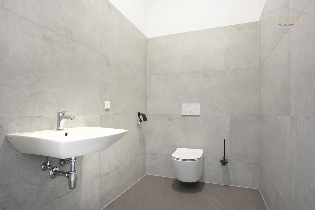 Modernes Gäste-WC mit wandhängender Toilette, Waschbecken und großformatigen grauen Fliesen.