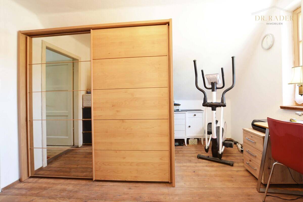 Vielseitiger Raum mit großem Holzschrank, Schreibtisch und Fitnessgerät.