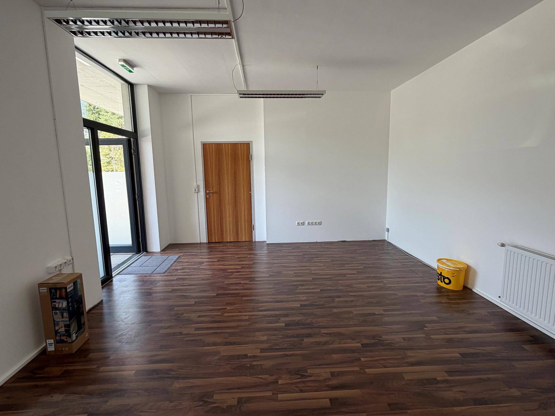 Heller Gewerberaum mit Holzboden, weißen Wänden und Zugang zur Außentür.