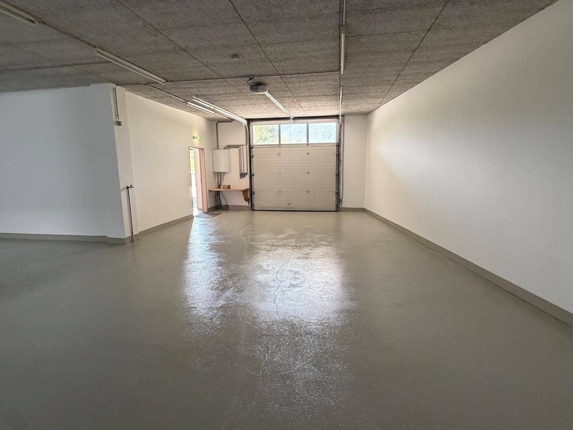 Heller Gewerberaum mit Rolltor und Betonboden, ideal für Lager oder Werkstatt.
