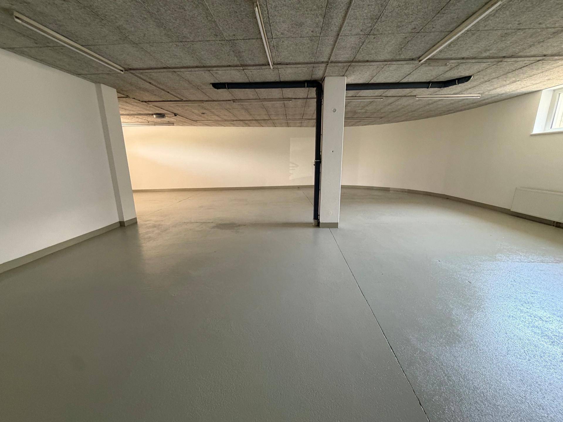 Geräumiger, leerer Gewerberaum mit grauem Betonboden und Deckenbeleuchtung.