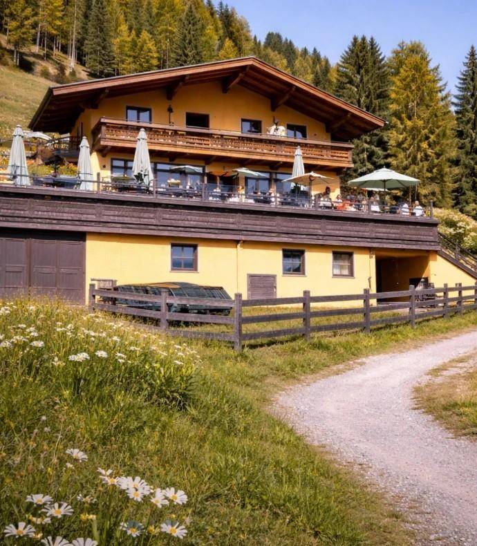 Gelbes Alpenhaus im Sommer mit großer möblierter Terrasse, umgeben von grünen Wiesen und Bäumen.