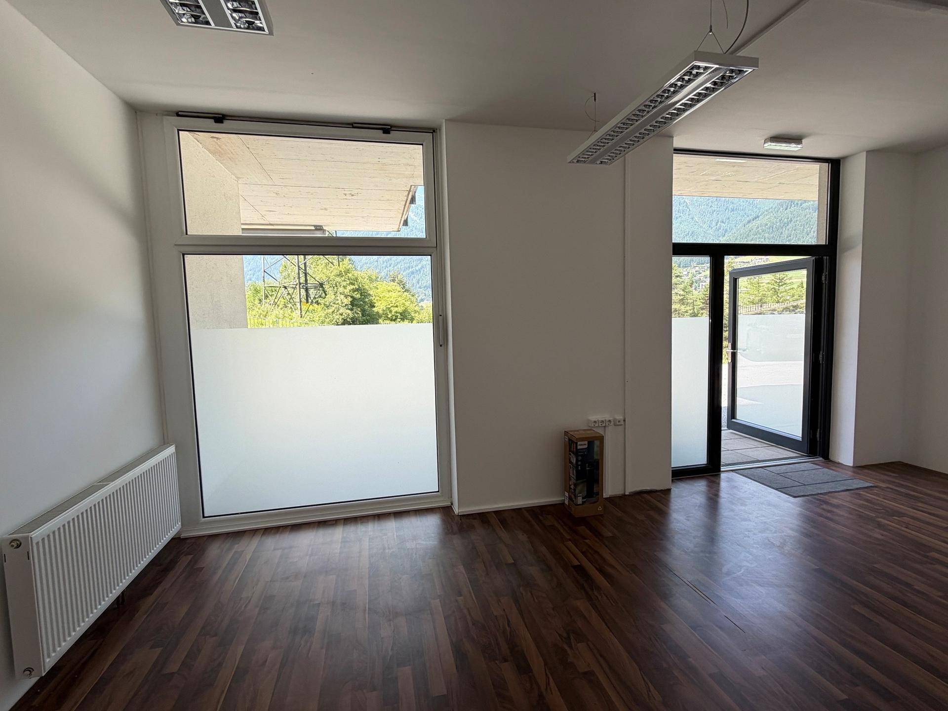 Innenansicht eines Gewerberaums mit großen Fenstern und dunklem Laminatboden.