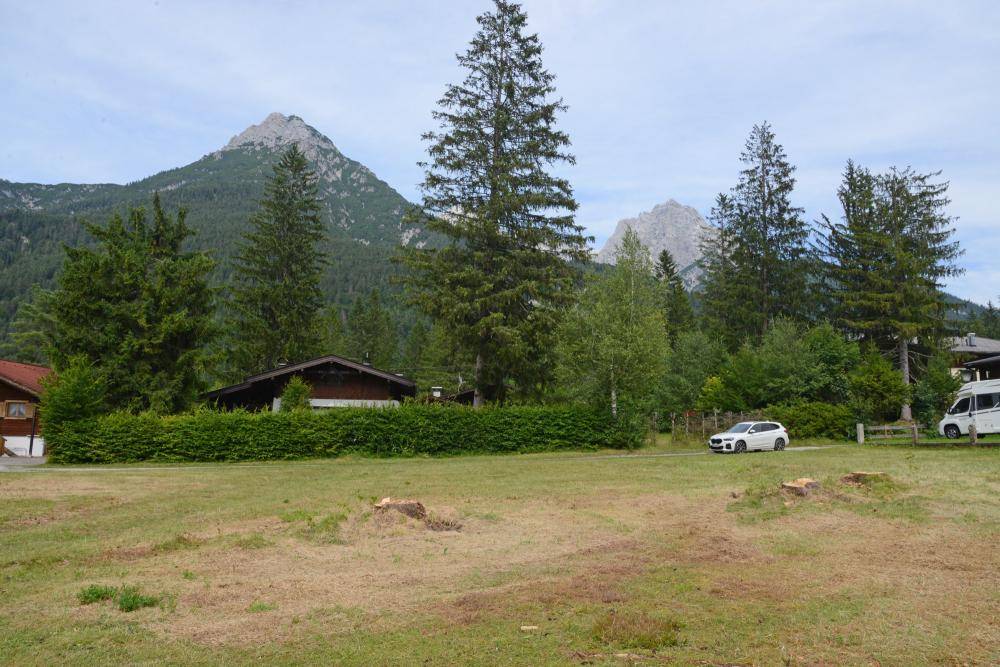 Offenes Feld mit Bergblick, umgeben von Bäumen und traditionellen Häusern, inklusive Zufahrt.