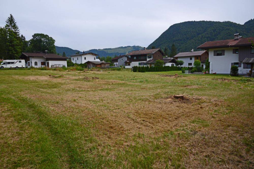 Weitläufige Wiese mit Blick auf eine Siedlung von Häusern und bewaldete Hügel in der Ferne.
