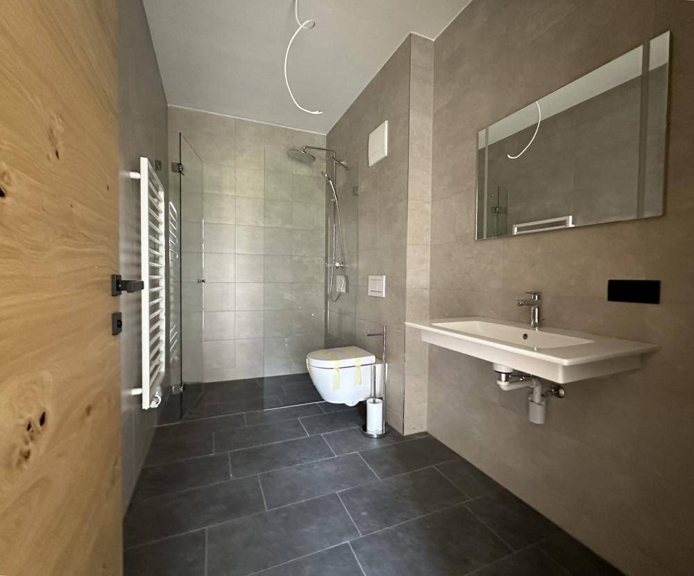 Modernes Badezimmer mit grauen Fliesen, ebenerdiger Dusche und Wand-WC.
