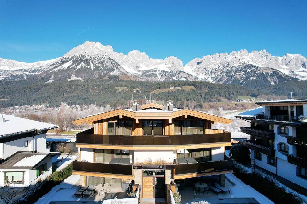 Architektonisch ansprechendes Gebäude mit Holzfassade und großen Glasflächen vor winterlicher Bergkulisse.